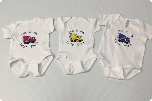 Three custom baby onesies saying this is my first shirt, and a cement truck in the middle